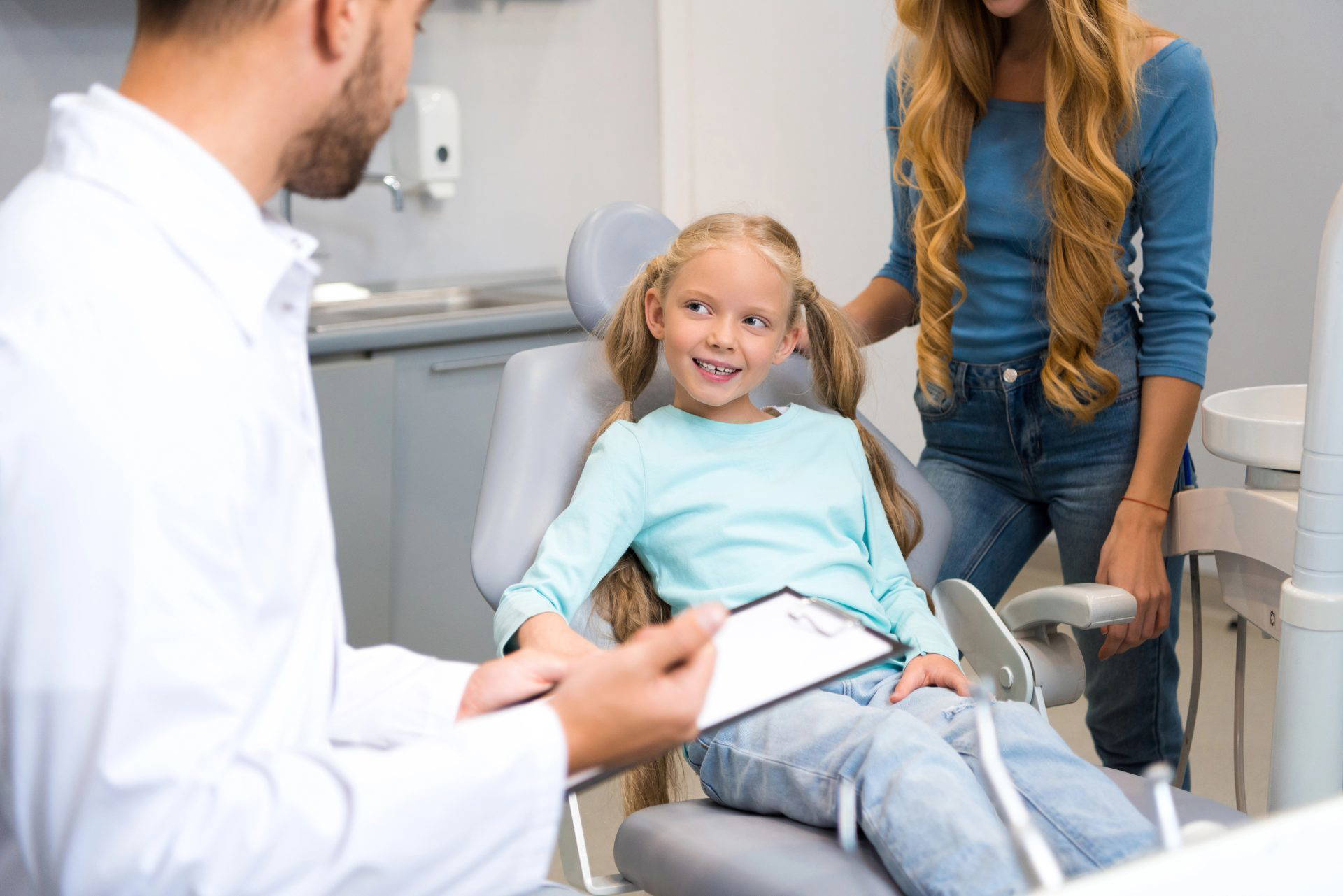Young girl sitting in a dental chair smiling, with a parent beside her