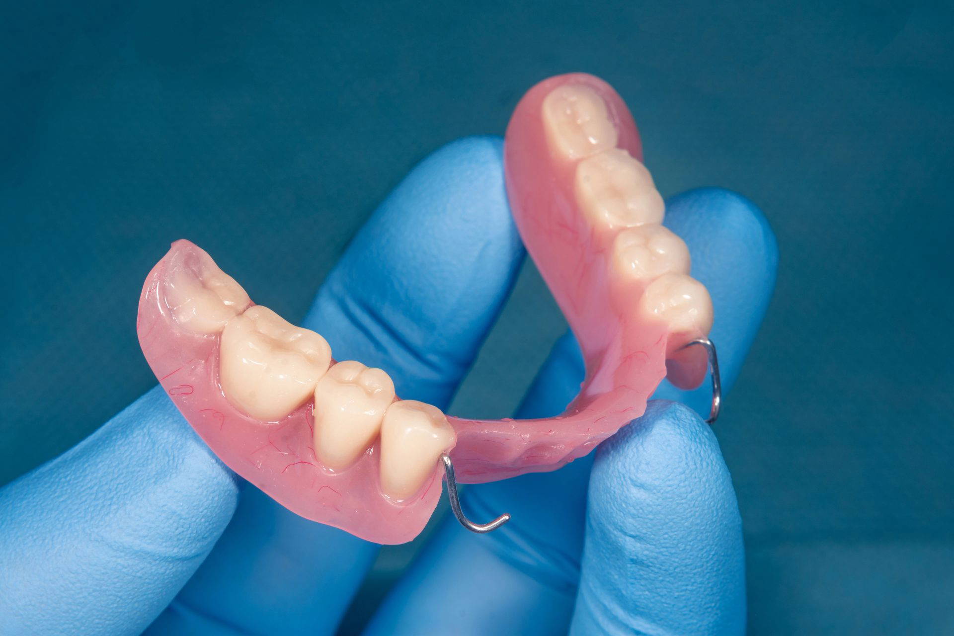 A set of dentures being held up by a dentist against a blue background
