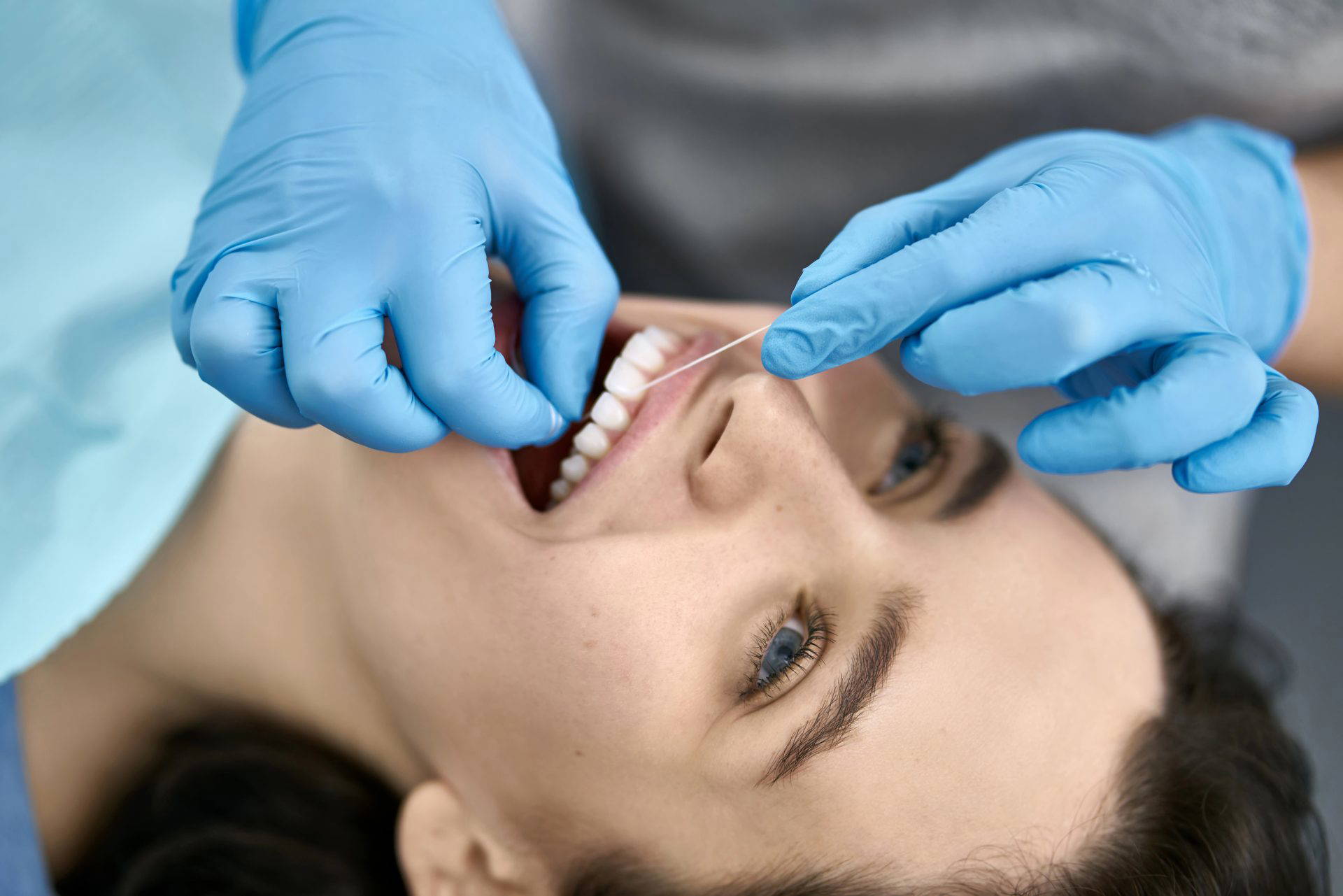 A woman smiling while a dentist flosses her teeth.