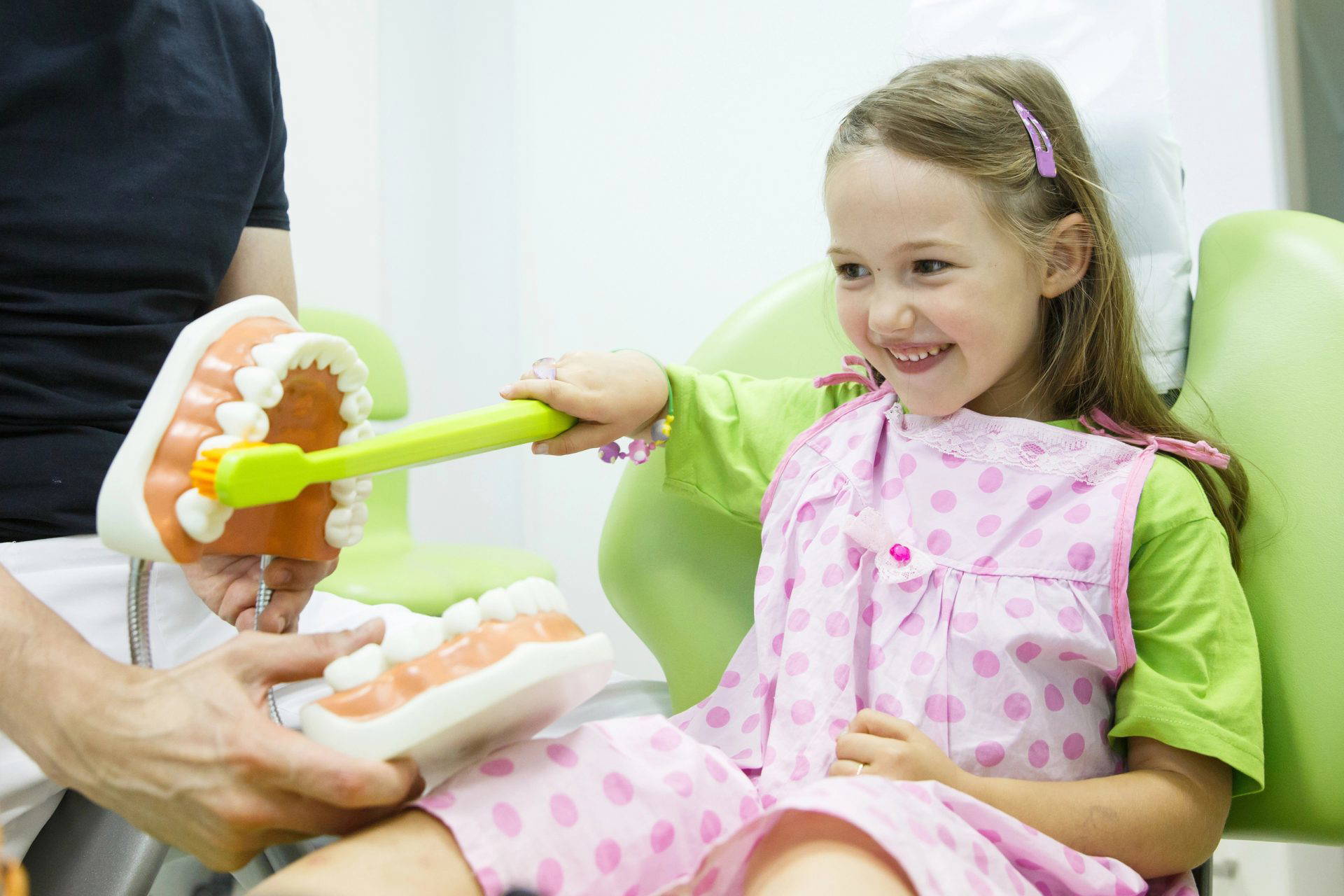 A young girl brushing the teeth of a demonstration piece.